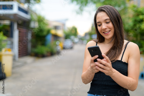 Young happy multi-ethnic woman using phone outdoors