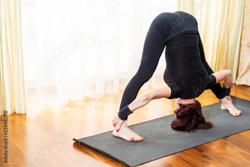 Woman Practicing Yoga Exercise Indoors At Bright Afternoon. Sitting in Prasarita Padottanasana Pose During Solitude Meditation Session. Wearing Black Top Shirt  and Black Leggings photo