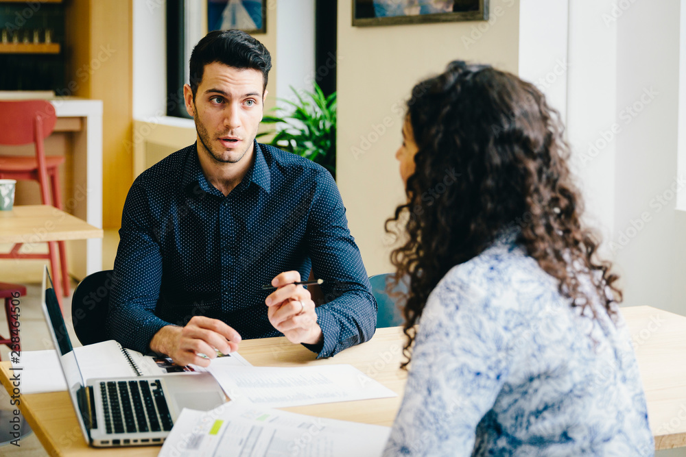 Businessman discussing business plan with female colleague while sitting at desk in office Businessman discussing business plan with female colleague while sitting at desk in office