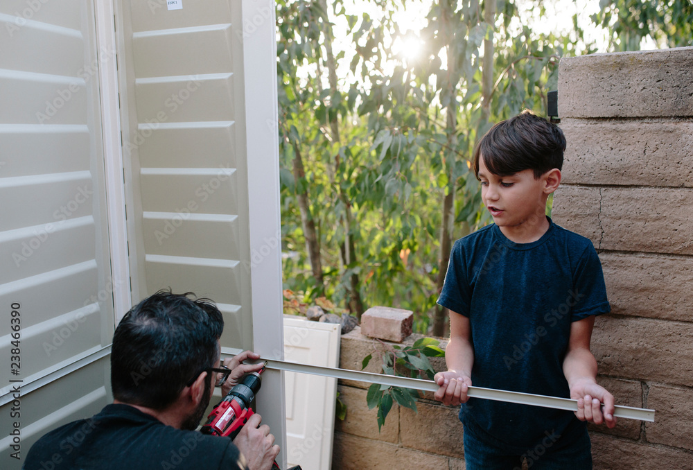 Son assisting father in drilling metal on door Son assisting father in drilling metal on door