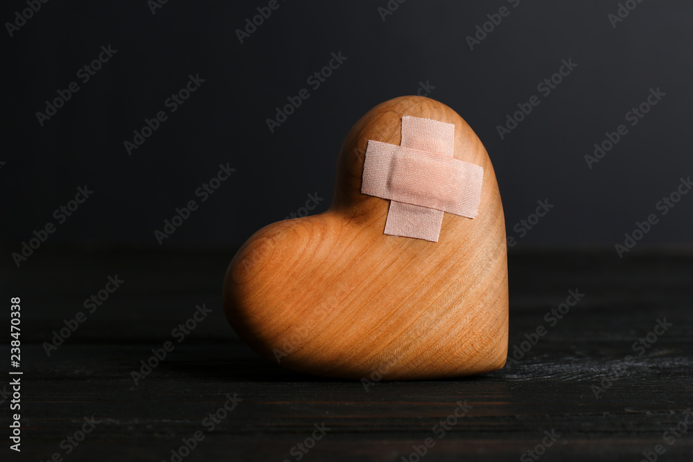 © New Africa - Wooden heart with adhesive plasters in darkness on table