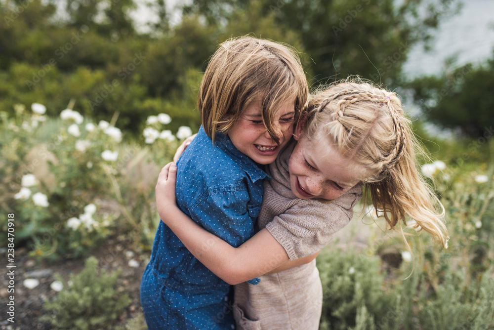 Happy sisters embracing while standing against plants in forest Happy sisters embracing while standing against plants in forest