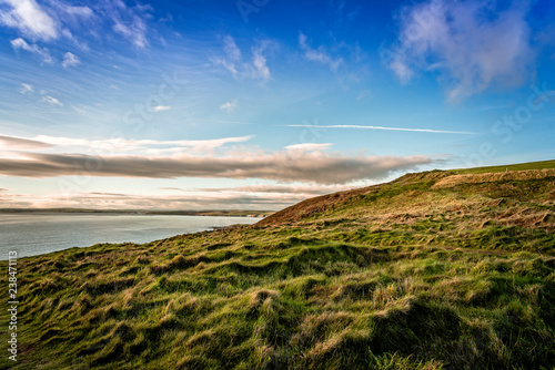 Scenic view of sea by green hill against blue sky during sunset