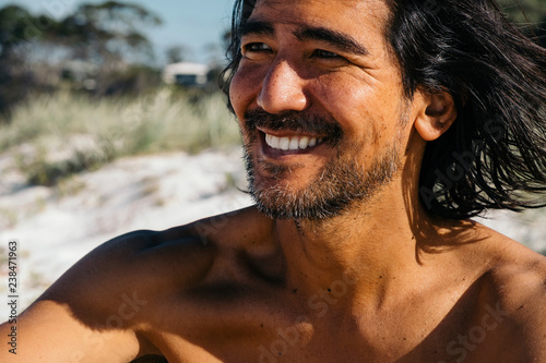 Close-up of happy shirtless man looking away while sitting at Hyams Beach during sunny day photo