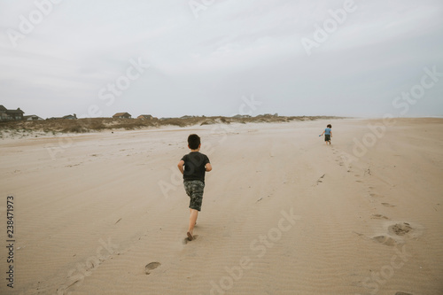 Rear view of boy running towards brother on beach