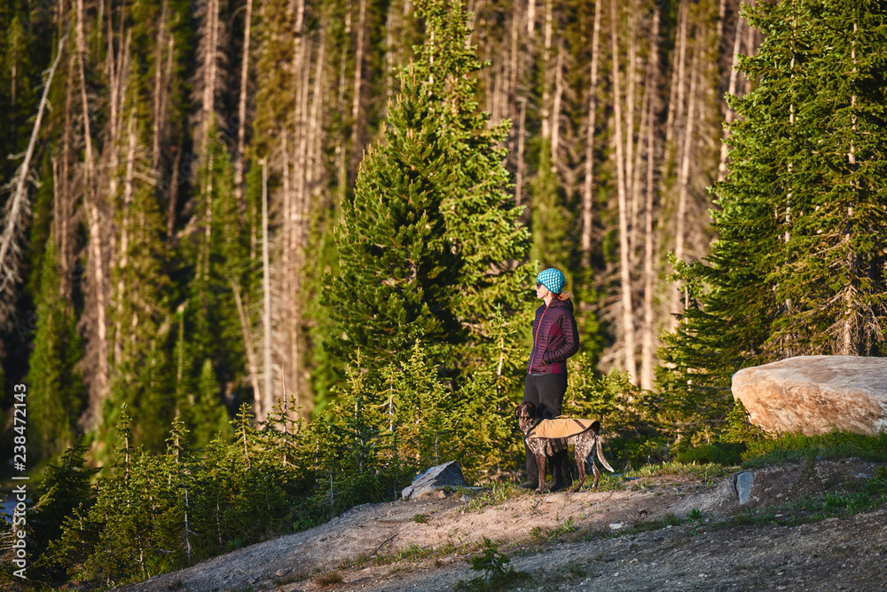 Obraz premium a young woman and her dog standing next to a beautiful mountain lake