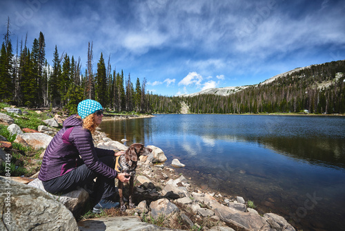 a young woman and her dog sitting next to a beautiful mountain lake