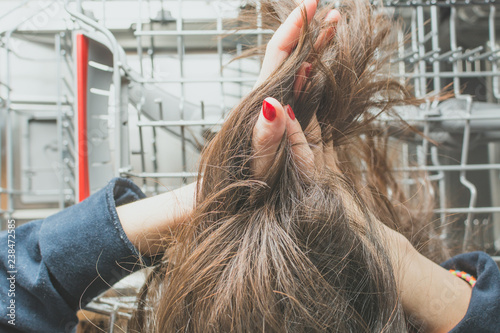 Фотография Girl lays long greasy hair in the dishwasher compartment