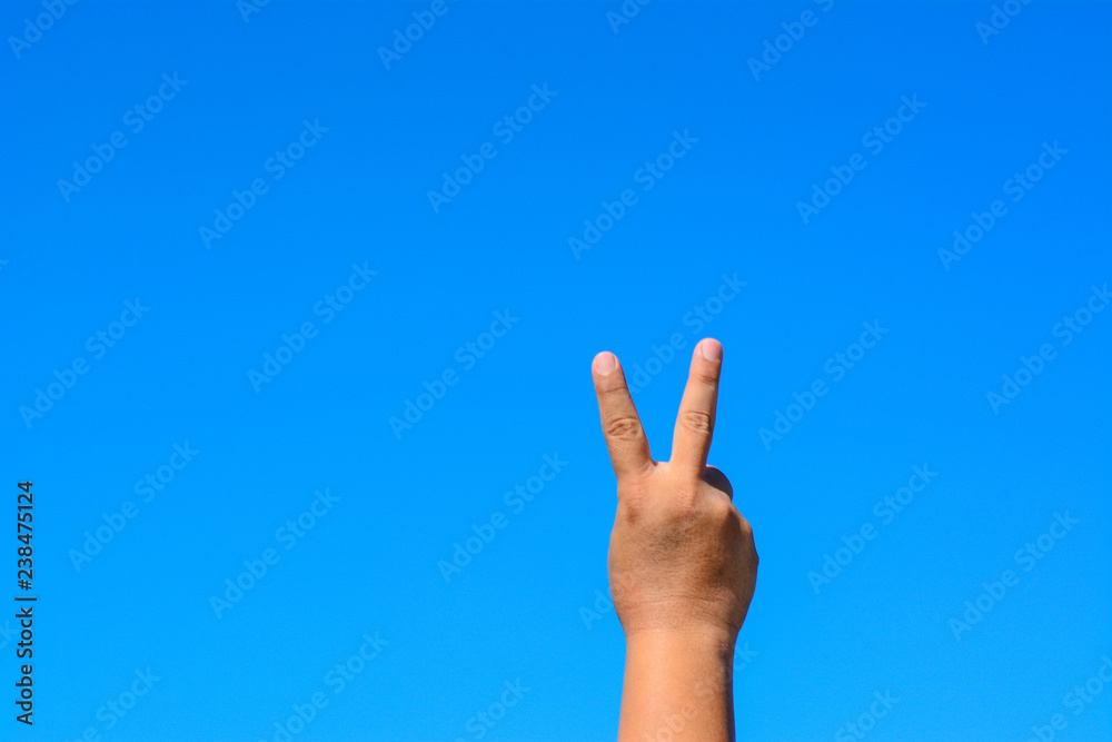 A male hand shows a peace symbol sign with two fingers isolated against blue sky background. A male hand shows a peace symbol sign with two fingers isolated against blue sky background.