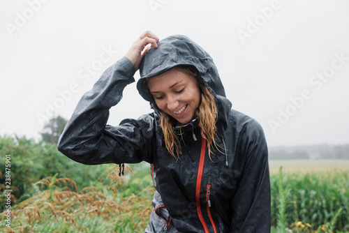 Happy woman in raincoat standing amidst plants against sky during rainy season
