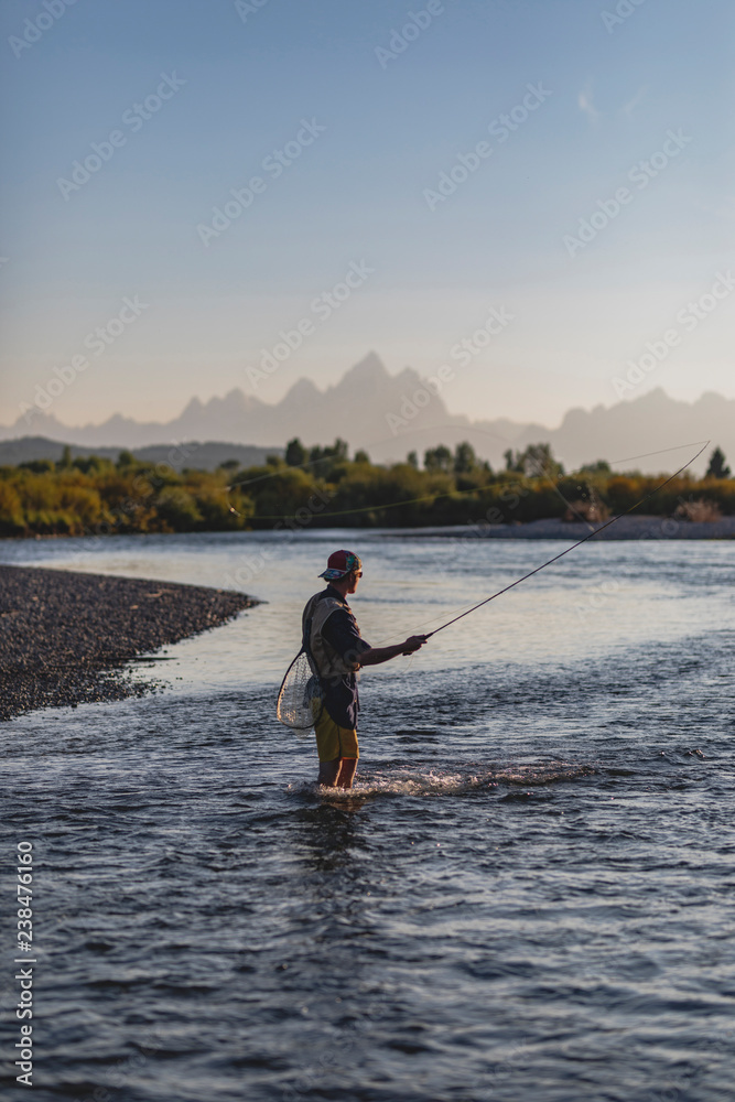 Side view of man fishing while standing in lake against clear sky during sunset Side view of man fishing while standing in lake against clear sky during sunset