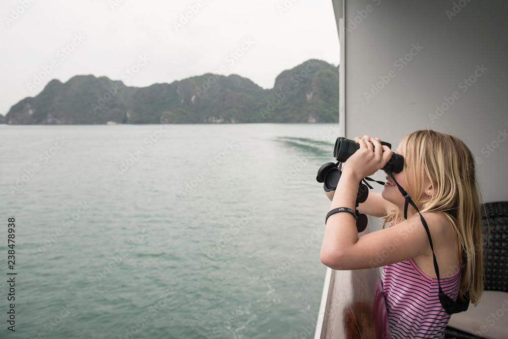 Side view of girl looking through binoculars while standing in boat on sea against sky Side view of girl looking through binoculars while standing in boat on sea against sky