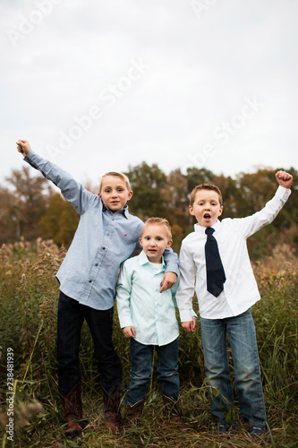 Portrait of happy brothers standing on grassy field against clear sky in forest photo