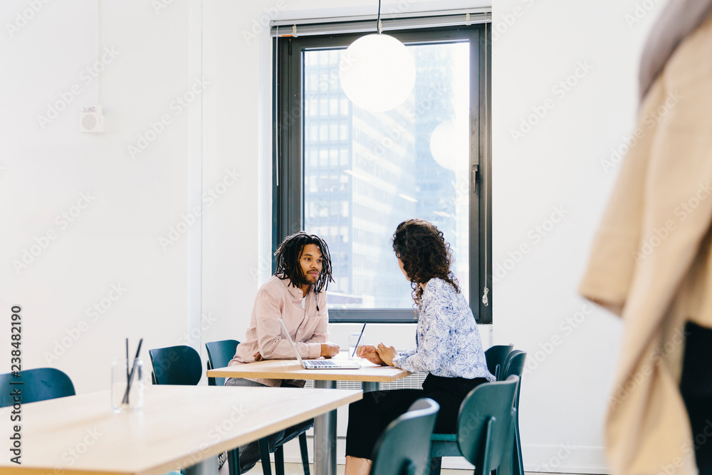 Businesswoman discussing with businessman while sitting at desk in office Businesswoman discussing with businessman while sitting at desk in office