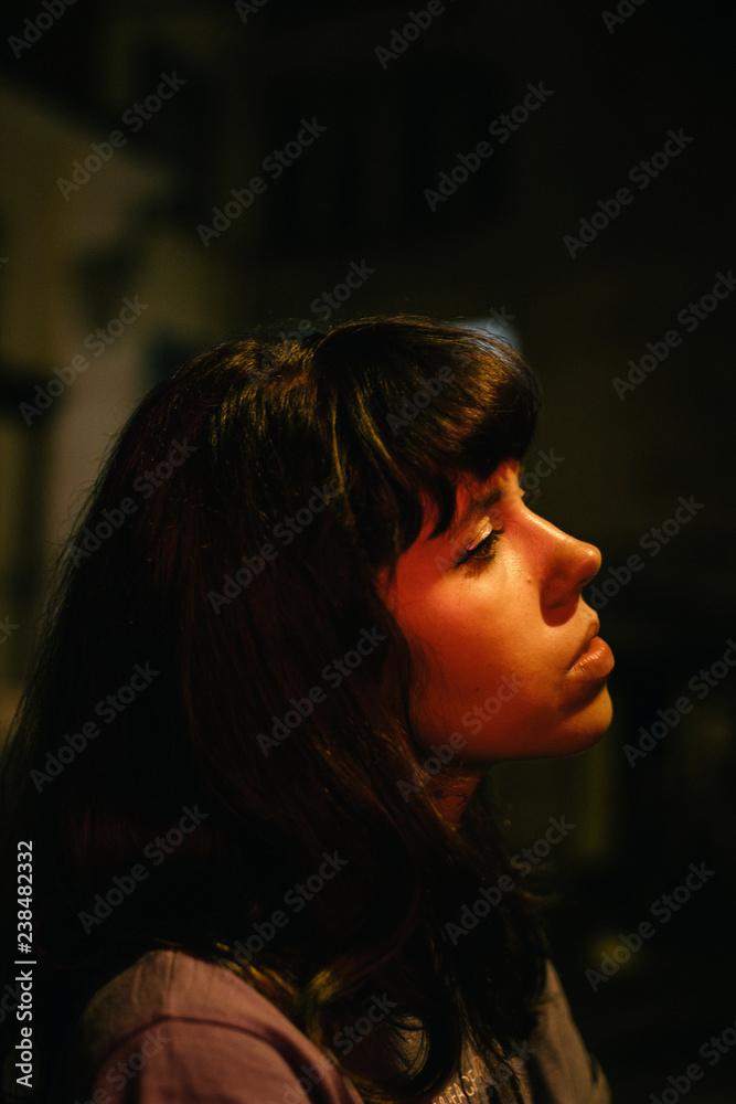 Side view of sad thoughtful woman looking away while sitting in darkroom Side view of sad thoughtful woman looking away while sitting in darkroom