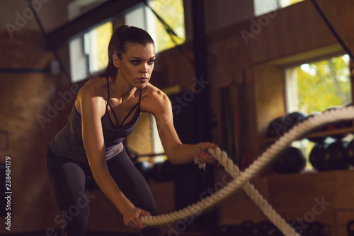 Fit, sporty and athletic sportswoman working in a gym. Woman training using battle ropes. Sports, athletics and fitness concept.