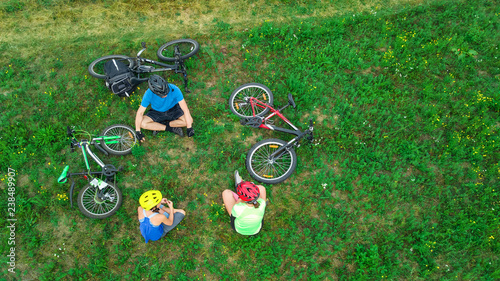 Family cycling on bikes outdoors aerial view from above, happy active parents with child have fun and relax on grass, family sport and fitness on weekend
