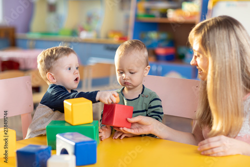Cute babies play with blocks. Educational toys for preschool and kindergarten child. Little boys and educator build block toys at playroom or daycare. Education concept.