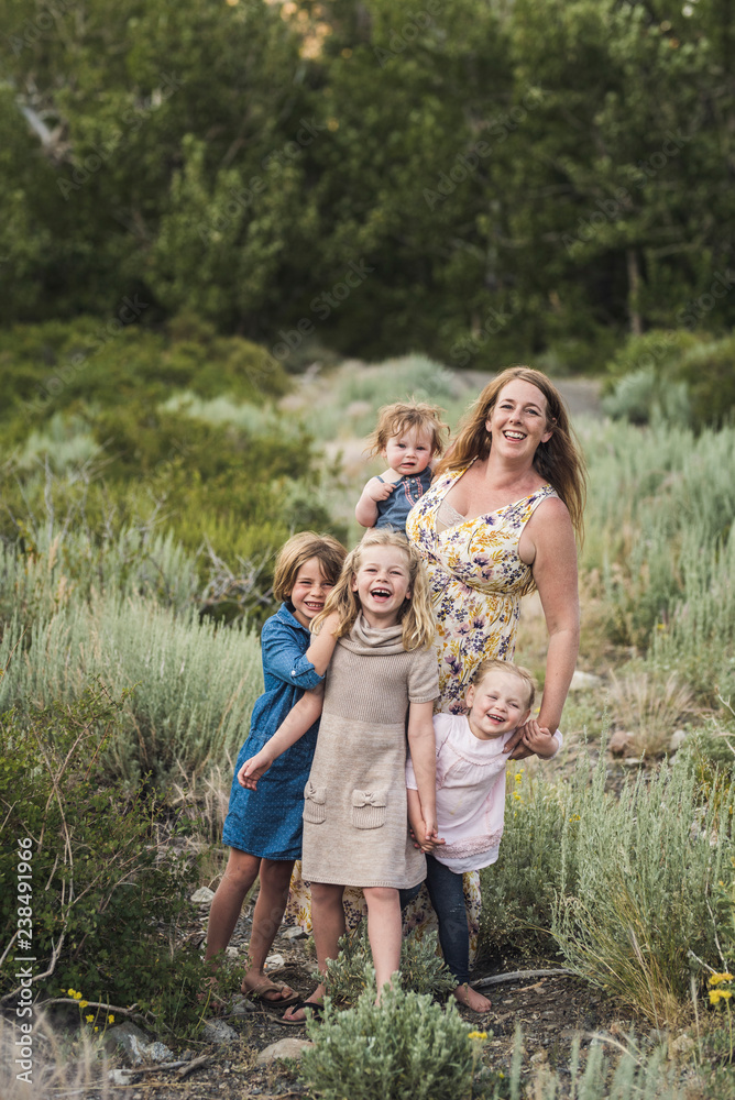 Portrait of happy mother with cute daughters standing on field amidst plants in forest Portrait of happy mother with cute daughters standing on field amidst plants in forest