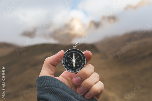 A male Hiker is looking for a direction with a magnetic compass in the mountains in the fall. Point of view shot. Man's hand with a watch bracelet holds a compass photo