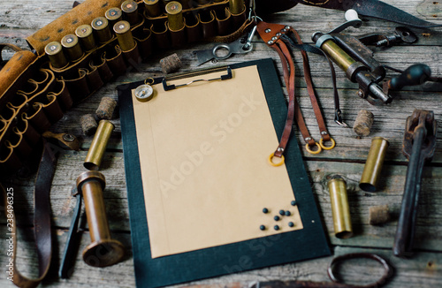 Clipboard with paper on old wooden background. Hunting equipment on vintage desk. Hunting belt with cartridges, top view