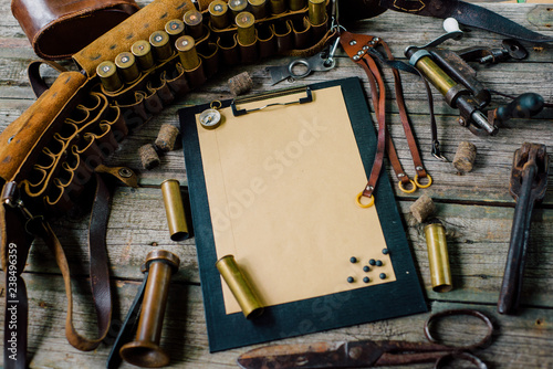 Clipboard with paper and pellets on it on old wooden background. Hunting equipment on vintage desk. Hunting belt with cartridges. Top view