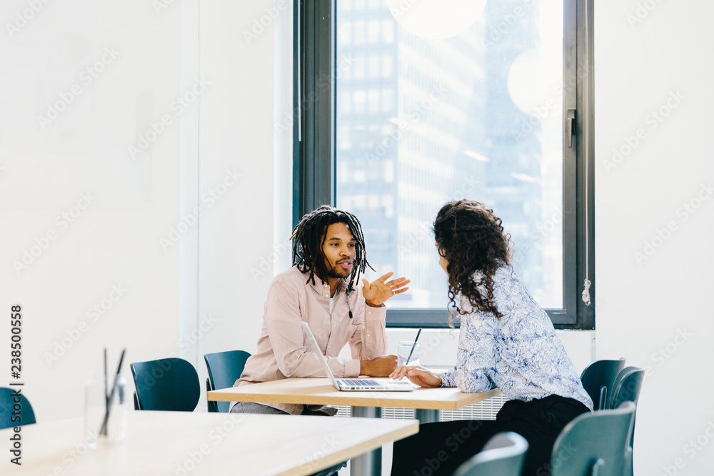 Businesswoman discussing with businessman while sitting at desk in creative office Businesswoman discussing with businessman while sitting at desk in creative office