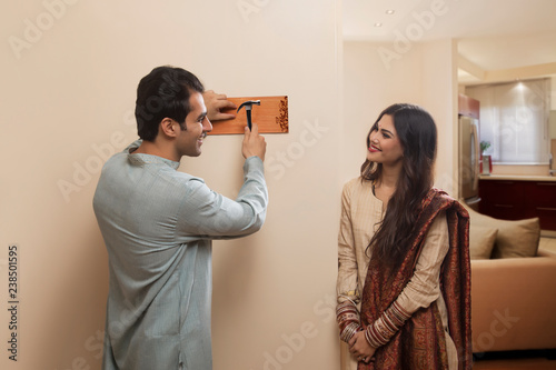 Young couple newlywed in traditional dress placing name plate to home	 photo