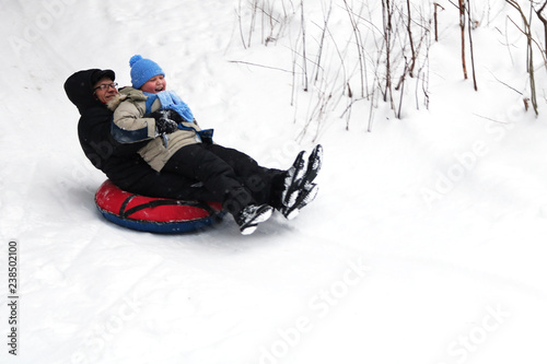 The father with the son ride the tubing from the hill.