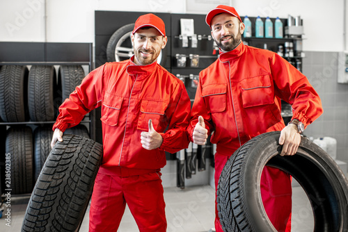 Portrait of a two car service workers in red uniform standing together with new tires at the store photo