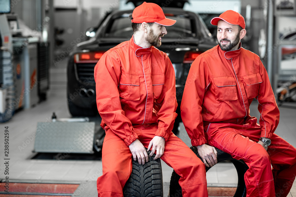 Car service workers in red uniform having a break sitting together on the wheels at the tire mounting service Car service workers in red uniform having a break sitting together on the wheels at the tire mounting service