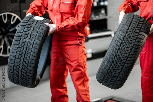 Worker in uniform carrying new tires at the car service or store, close-up view
