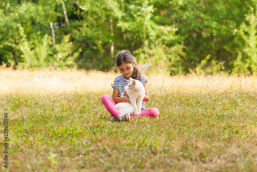 Girl with white cat sitting on grass outdoors