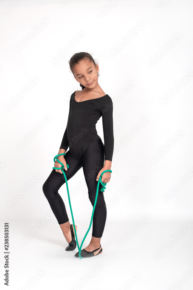 Foto de Studio shot of attractive little gymnast girl of wearing black  leggings and a bathing suit with a green jump rope on a white background,  full length. do Stock