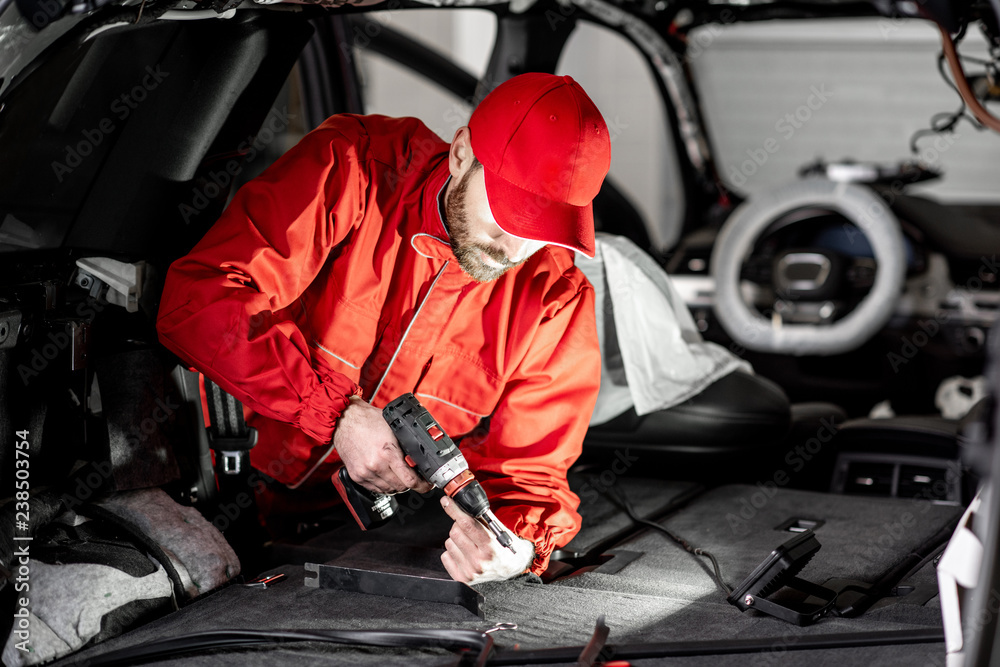 Fototapeta premium Handsome auto service worker in red uniform disassembling new car interior making some improvements