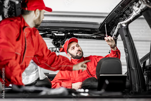 Two auto service workers in red uniform disassembling new car interior making some improvements indoors © rh2010