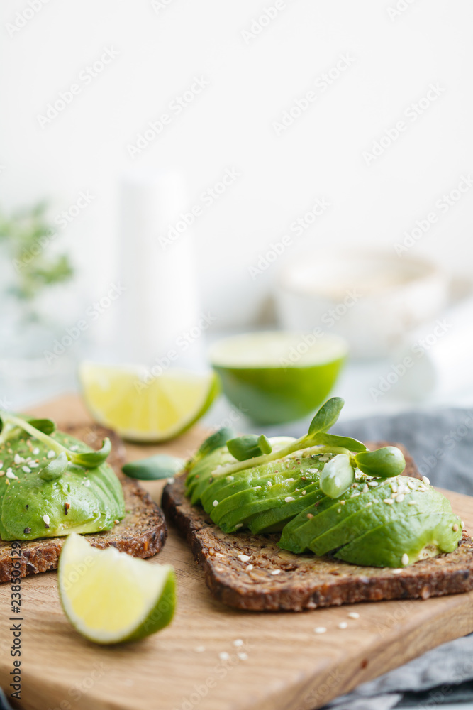 Two toasts with avocado on a wooden board on a breakfast table. The concept of vegetarian and healthy diet food.