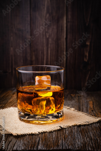 Whiskey with ice cube in a glasses on a rustic dark wooden table