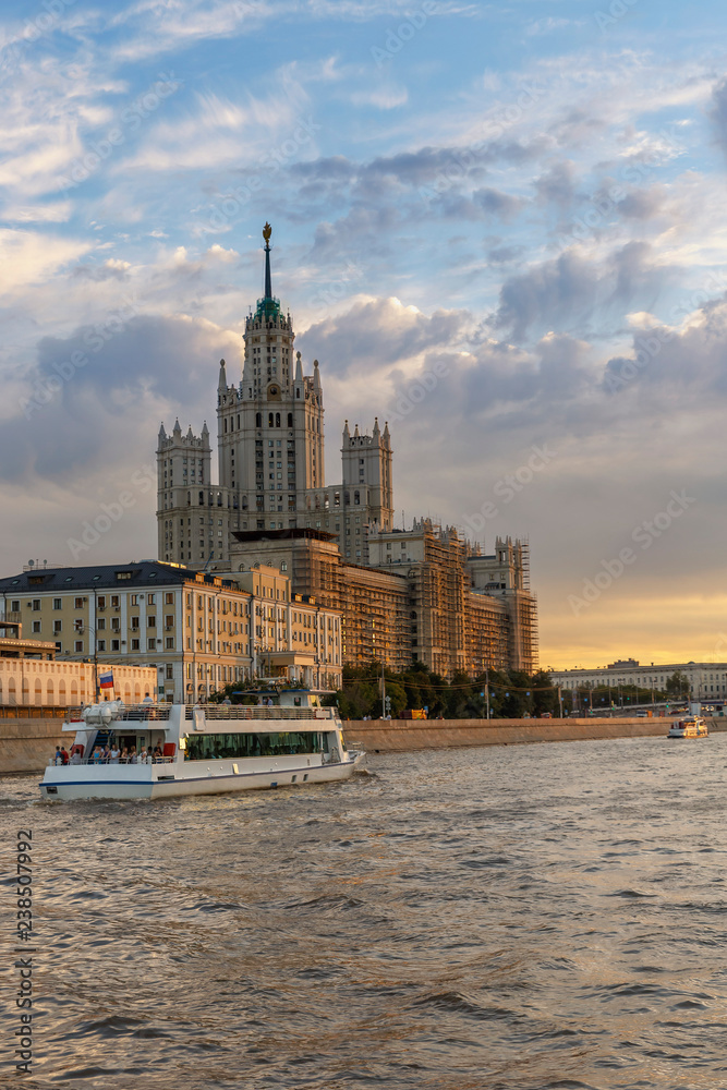 General view of the Moscow River with a tourist ship and a high-rise building on the background of a beautiful evening sky