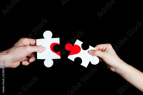 Puzzle with a red heart in the hands of a loving couple. Valentine's Day concept. Torn heart.On a black background