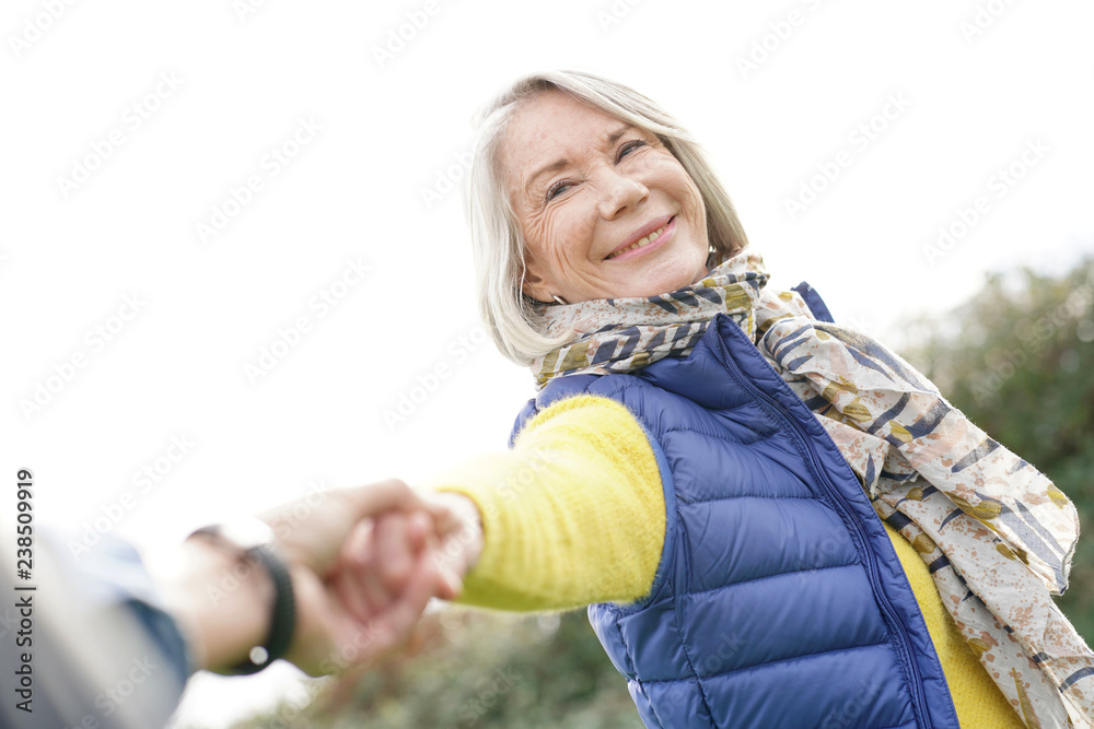  Portrait of vibrant senior woman holding partner's hand and pulling him along outdoors - obrazy, fototapety, plakaty 