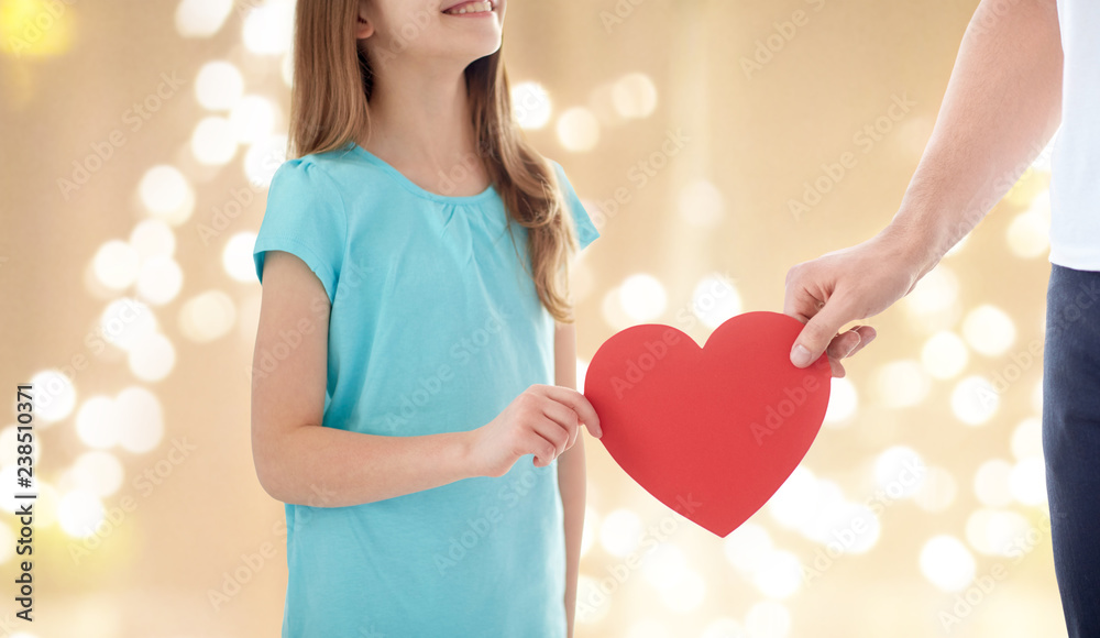 love, charity and family concept - close up of girl and father hand holding red heart shape over festive lights background