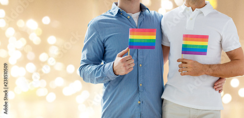 gay pride, homosexuality and lgbt concept - close up of happy male couple hugging and holding rainbow flags over festive lights background