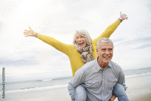 Modern vibrant senior couple piggy back riding on beach photo