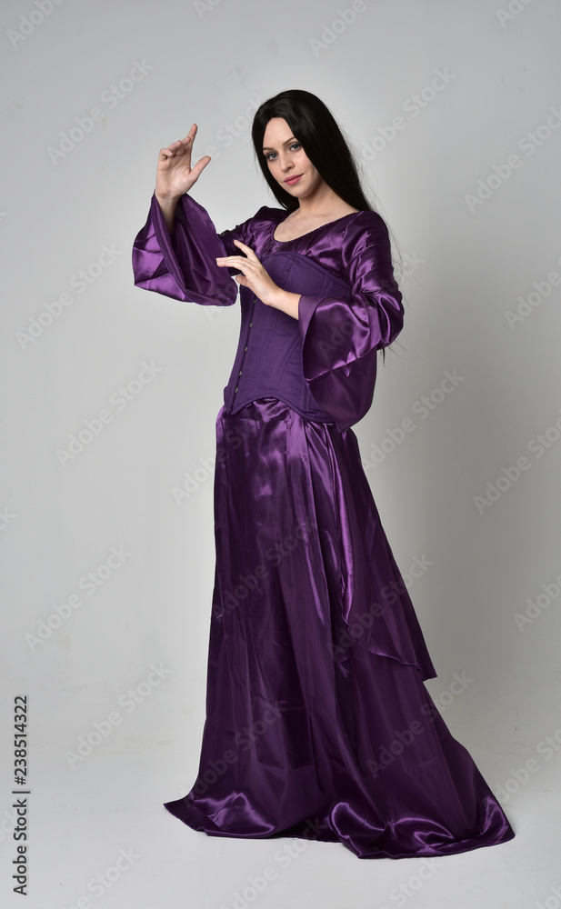 full length portrait of beautiful girl with long black hair, wearing purple fantasy medieval gown. standing pose on grey studio background. full length portrait of beautiful girl with long black hair, wearing purple fantasy medieval gown. standing pose on grey studio background.