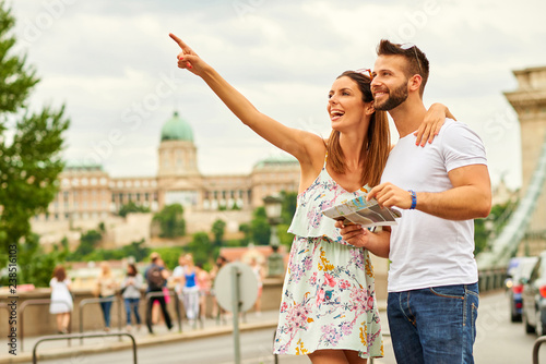 A beautiful young woman is pointing away while her boyfriend is holding a map with the castle of Buda and the Chain Bridge behind them in Budapest, Hungary.  © Spectral-Design