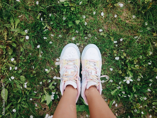 Legs in white sneakers on spring green grass