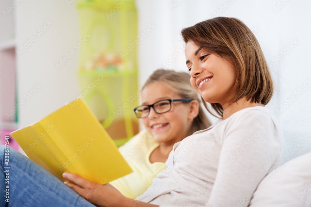 people, family and education concept - happy daughter with mother reading book at home