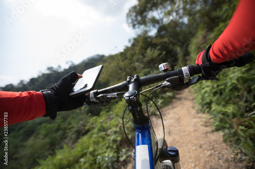 Riding on top of hill, holding mobile phone, using online application for searching GPS coordinates while riding bike in forest on sunny day © lzf