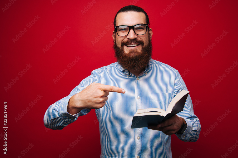 Cheerful bearded man wearing glasses and pointing at open book Cheerful bearded man wearing glasses and pointing at open book